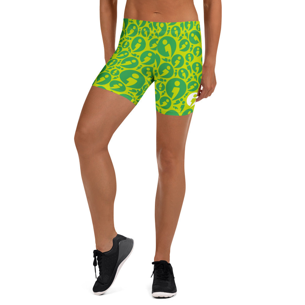A person pictured from torso below wearing The Movement Collection's fitted shorts in the green color variant featuring green semi-colon avatar randomly placed over a light green background.