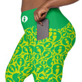 Close-up of a person wearing bright green and yellow leggings with an allover Still I Run avatar pattern and a side pocket holding a phone. A white logo is visible on the waistband.