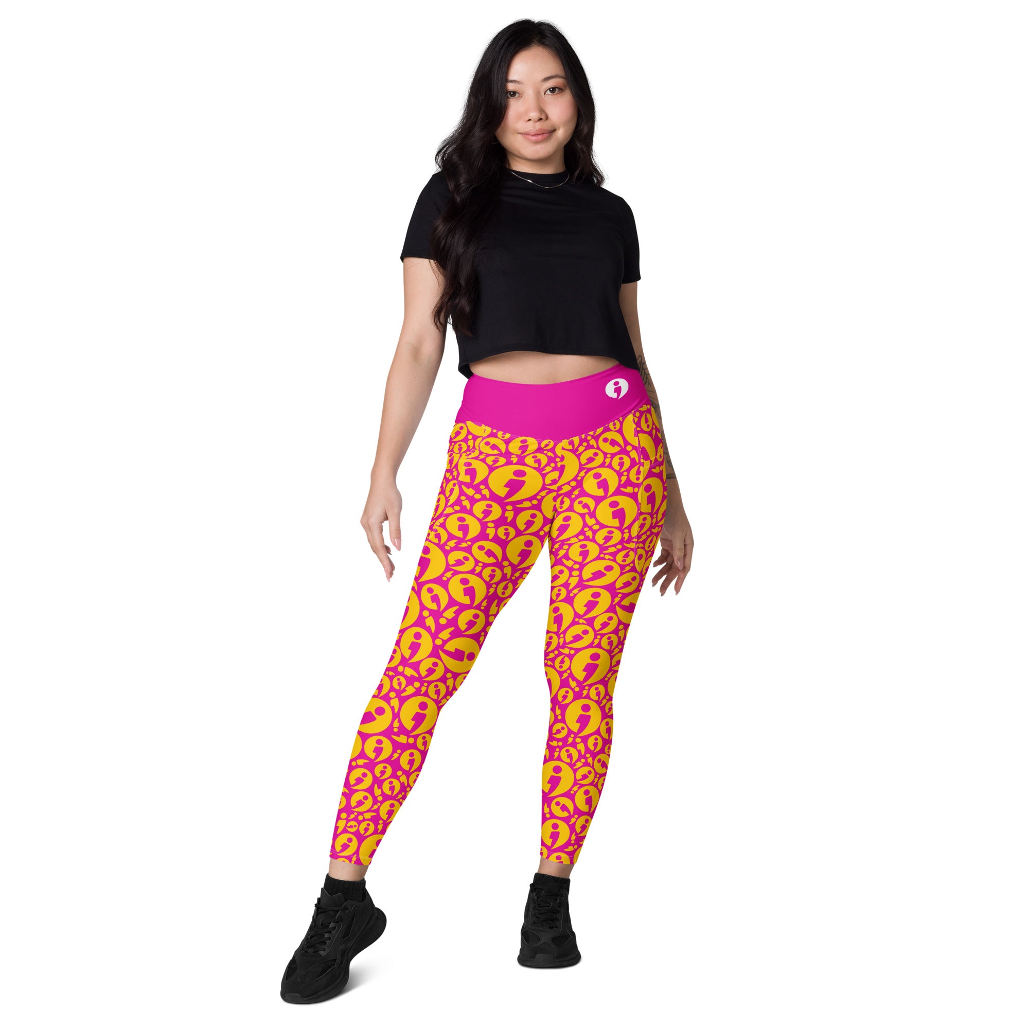 A woman modeling high-waisted leggings with a bright pink Avatar pattern, paired with a black crop top and black sneakers, on a solid white background.