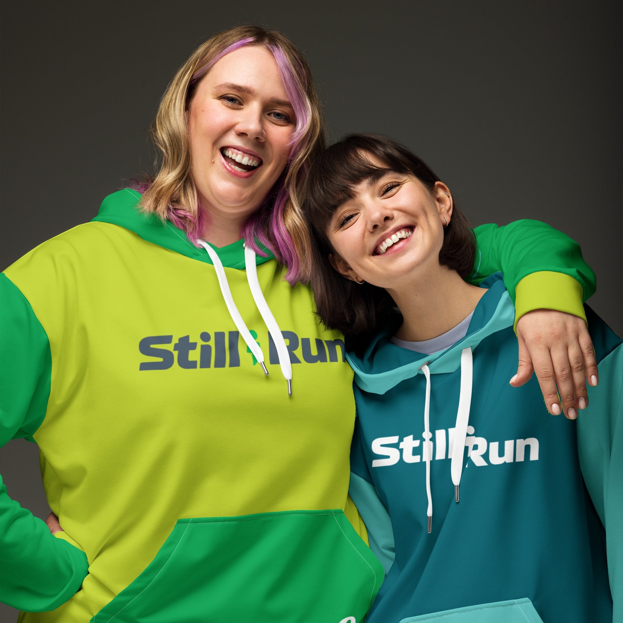Two people wearing the Movement Collection unisex hoodies. Both feature the 'Still I Run' logo. The person on the left is wearing the green color variant and the person on the right is wearing the teal color variant.