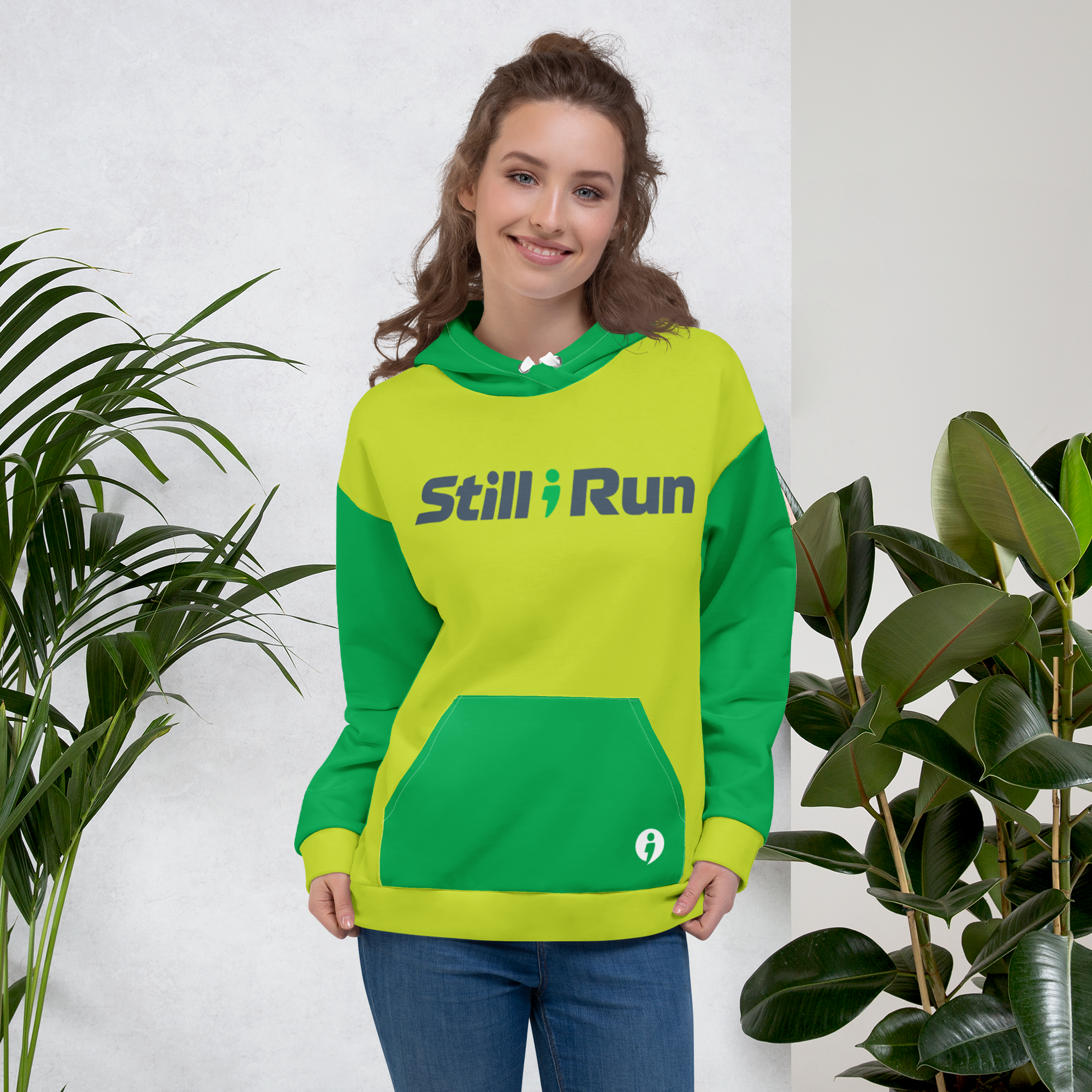 A person wearing the green Movement Collection hoodie with the 'Still I Run' logo across the front and a white avatar featured on the bottom right side of the hoodie pocket.