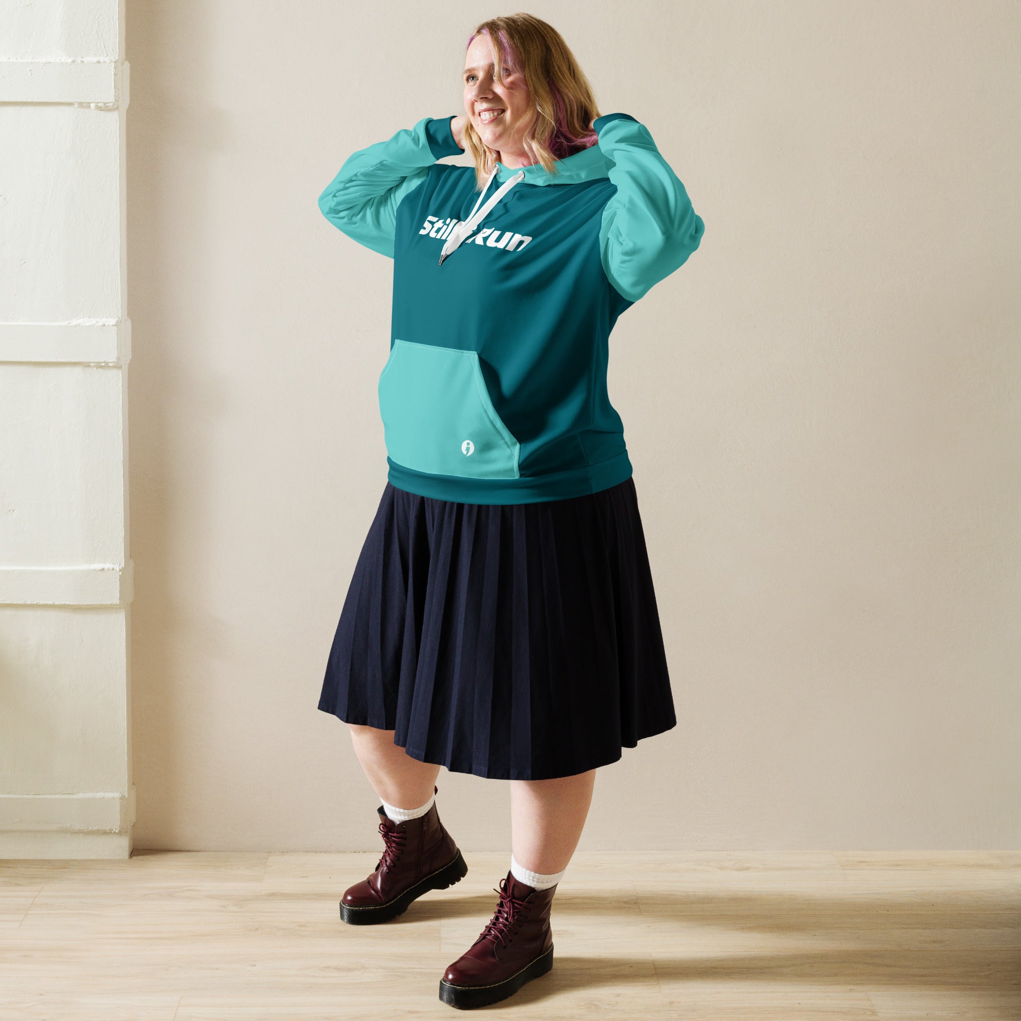 A woman wearing the teal Movement Unisex Hoodie with her arms up as if to pull the hood up over her head.